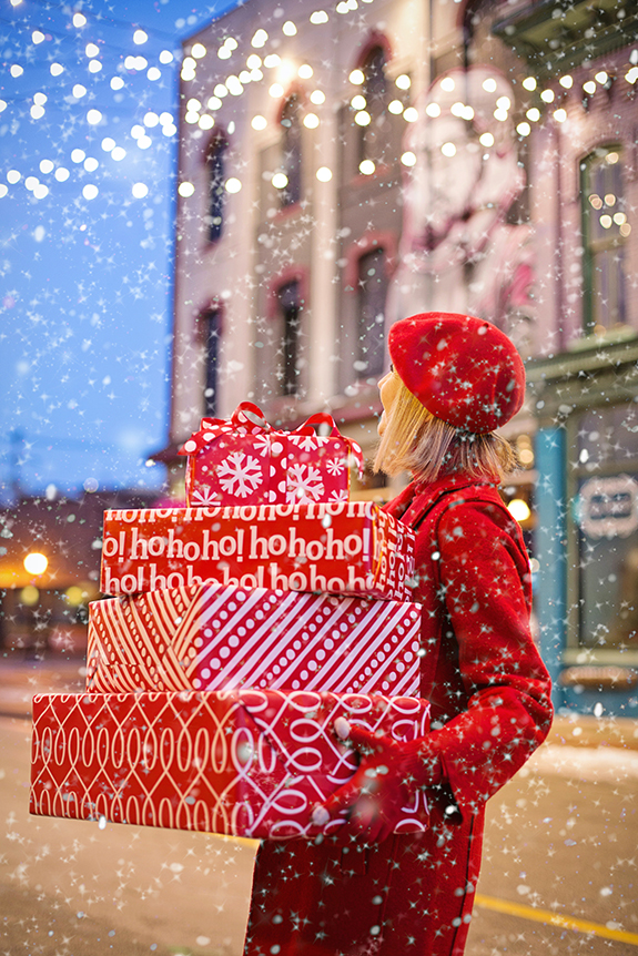 Girl in red carrying Christmas gifts in red & white wrapping paper.